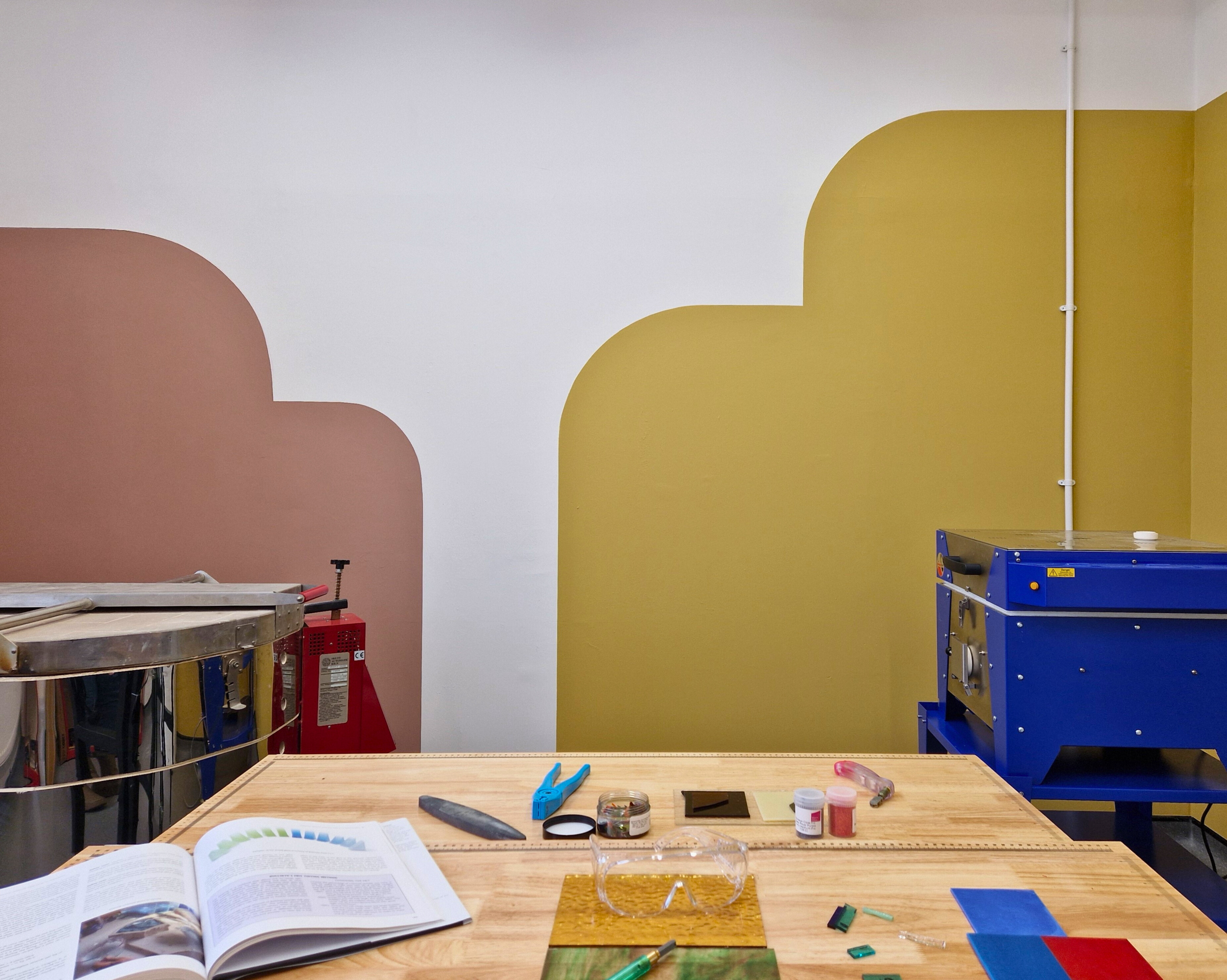 Culture Perth & Kinross - Image of kiln room at Perth Creative Exchange. A ceramics kiln on the left and a blue glass kiln on the right with pink and yellow paint on the wall and a workbench in the foreground