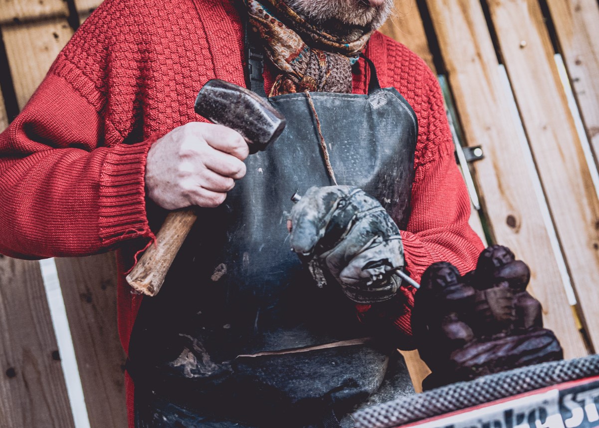 City of Craft 6 Culture Perth & Kinross - Close up of stone carver about to hit a chisel with a hammer, working on a small decorative stone carving of two people